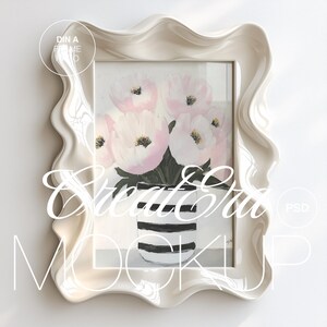 Peut inclure: Cadre en céramique blanche avec un bord ondulé, présentant une peinture de fleurs roses dans un vase rayé noir et blanc. Le cadre est une maquette pour l'affichage d'œuvres d'art.