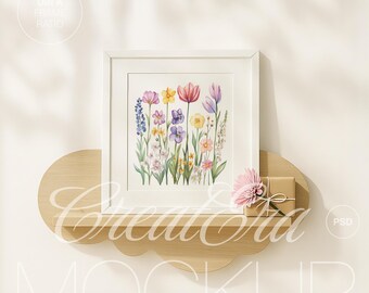 May include: A white framed print featuring a watercolor painting of colorful flowers, including tulips, daffodils, and pansies. The print is displayed on a cloud-shaped wooden shelf, with a small gift box and a pink flower.
