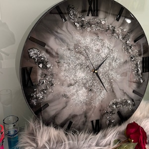 May include: A black and white resin clock with silver glitter embedded in the resin. The clock face has Roman numerals and black hands. The clock is on a white faux fur surface with a red rose.