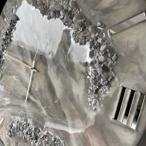 May include: A gray and white resin clock face with silver accents and embedded gray stones. The clock face has Roman numerals and a silver hand.