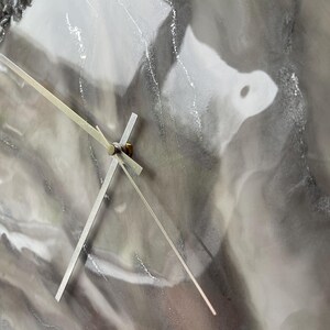 May include: A close-up of a gray and white resin clock face with silver hands. The clock face has a marbled, abstract design.