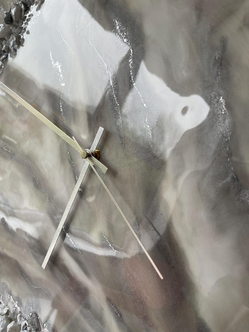 May include: A close-up of a gray and white resin clock face with silver hands. The clock face has a marbled, abstract design.