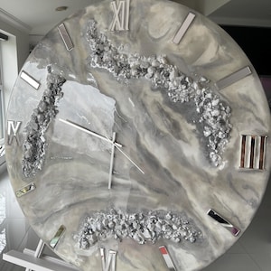 May include: A large, round, gray and white clock with Roman numeral markings and silver accents. The clock face has a marbled design with embedded silver glitter.