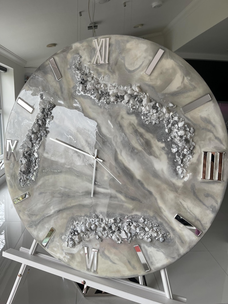 May include: A large, round, gray and white clock with Roman numeral markings and silver accents. The clock face has a marbled design with embedded silver glitter.