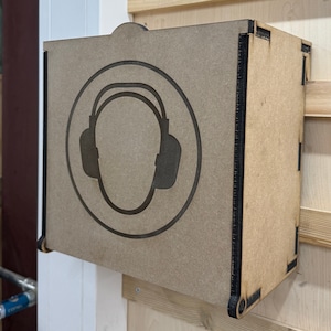 May include: A brown wooden box with a black silhouette of a person wearing earmuffs. The box is mounted on a wall.
