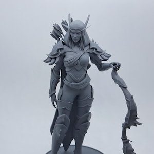 May include: A grey figurine of a female warrior, holding a bow. The figure is clad in detailed armour, with a flowing cape and a quiver of arrows on her back. The figurine stands on a circular base, showcasing intricate design elements.