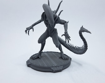 Puede incluir: Una figura gris de criatura extraterrestre impresa en 3D con una cola larga y un cuerpo segmentado. El extraterrestre está de pie sobre una base circular con una superficie texturizada.