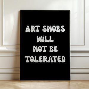 May include: A rectangular black wall art print in a thin black frame featuring the white text ART SNOBS WILL NOT BE TOLERATED in a bold, rounded, retro-inspired font. The design is centred on the black background, creating a high-contrast display.