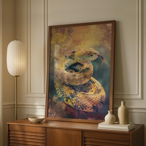 May include: A framed wall art print featuring a coiled snake with yellow and brown scales, a textured pattern, and a visible red tongue. The artwork is displayed in a dark wood frame, resting on a wooden cabinet alongside two ceramic vases.