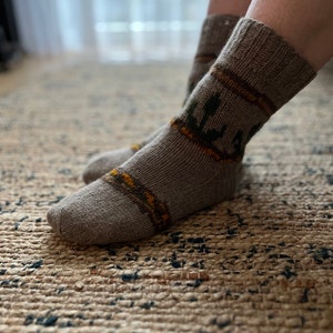 Puede incluir: Un par de calcetines de punto en tonos marrones, con un diseño estampado con detalles en verde y amarillo. Los calcetines son gruesos y parecen cálidos, adecuados para el clima frío. Los calcetines están sobre una alfombra texturizada.