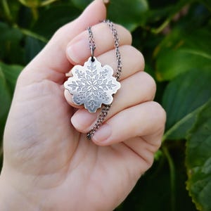 Op de afbeelding: Een zilveren sneeuwvlok hangerketting met een delicaat, ingewikkeld ontwerp. De hanger hangt aan een zilveren ketting.