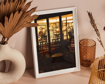 May include: A white framed photograph of a restaurant interior with a sign that reads "Service" and "Nouiller" in red letters. The photo is on a pink surface with a brown palm frond, a brown glass vase, a brown glass candle holder, and a gold metal wire basket.