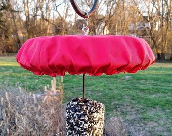 May include: A red fabric squirrel feeder cover with a black metal cage and a cylindrical birdseed cake hanging from a metal hook.