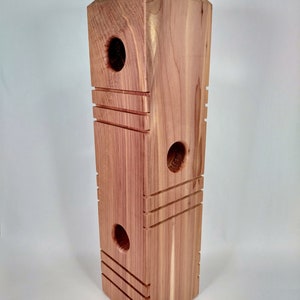 May include: A wooden bird feeder with three holes and a hanging loop. The feeder is made of cedar wood and has a natural wood finish.
