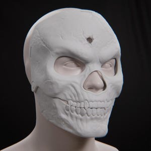 May include: A matte white skull mask featuring a textured, weathered surface with deep cracks and a prominent bullet hole indentation on the forehead. The mask covers the upper face, revealing the eyes and nose, with a detailed skeletal jaw.