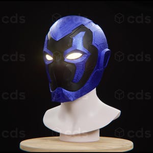 Puede incluir: Un casco azul y negro con una superficie texturizada y ojos brillantes. El casco está en un soporte blanco.