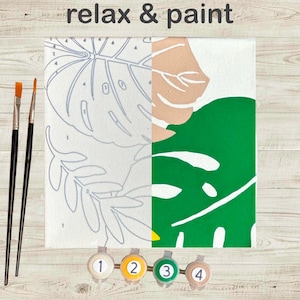 May include: A paint-by-numbers canvas with a tropical leaf design, partially painted in green, beige, and white. The words "relax & paint" are at the top. Includes paintbrushes and numbered paint pots.