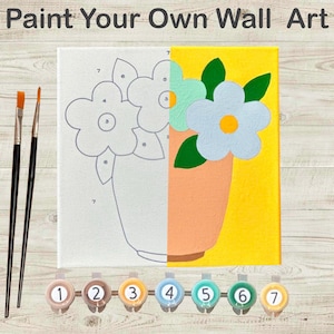 May include: A split canvas with a floral design, half outlined and half painted. The painted side features blue and green flowers in a peach vase against a yellow background. Paintbrushes and numbered paint pots are included. Text reads "Paint Your Own Wall Art."