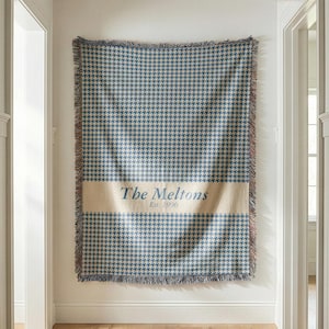 May include: A white ceramic mug with a black handle and the text "But First, Coffee" in a bold, black font. The mug is set against a blurred background, suggesting a cozy setting.