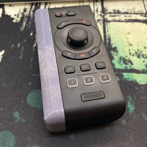 May include: A black remote control with a circular directional pad, four buttons labeled "P1", "P2", "P3", and "OBSBOT", and three buttons labeled "1", "2", and "3".