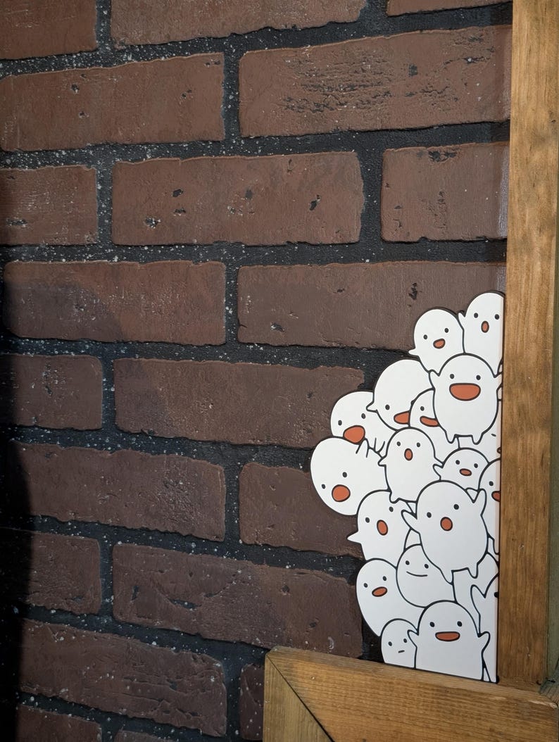 May include: A collection of white cartoon ghost stickers with orange mouths and black eyes. The stickers are clustered together, peeking out from behind a wooden frame. The background features a brick wall with dark brown bricks.