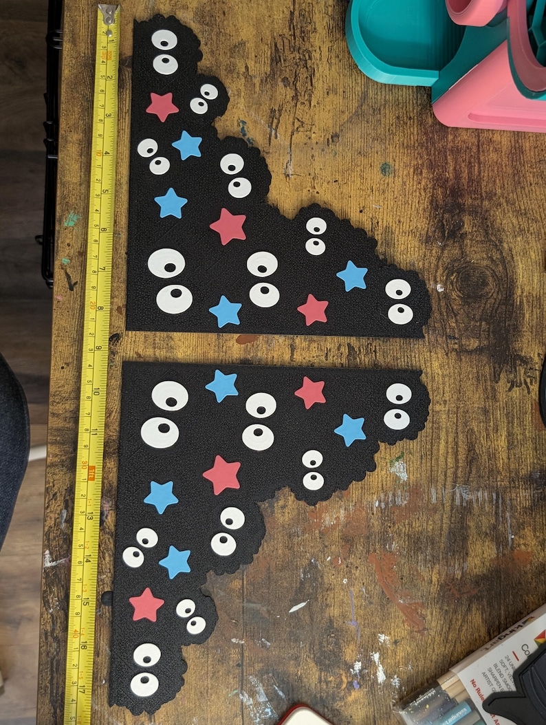 May include: Two black L-shaped foam pieces decorated with white cartoon eyes and red and blue stars. A yellow measuring tape is placed vertically along the left side, showing the pieces are approximately 17 inches in total length.