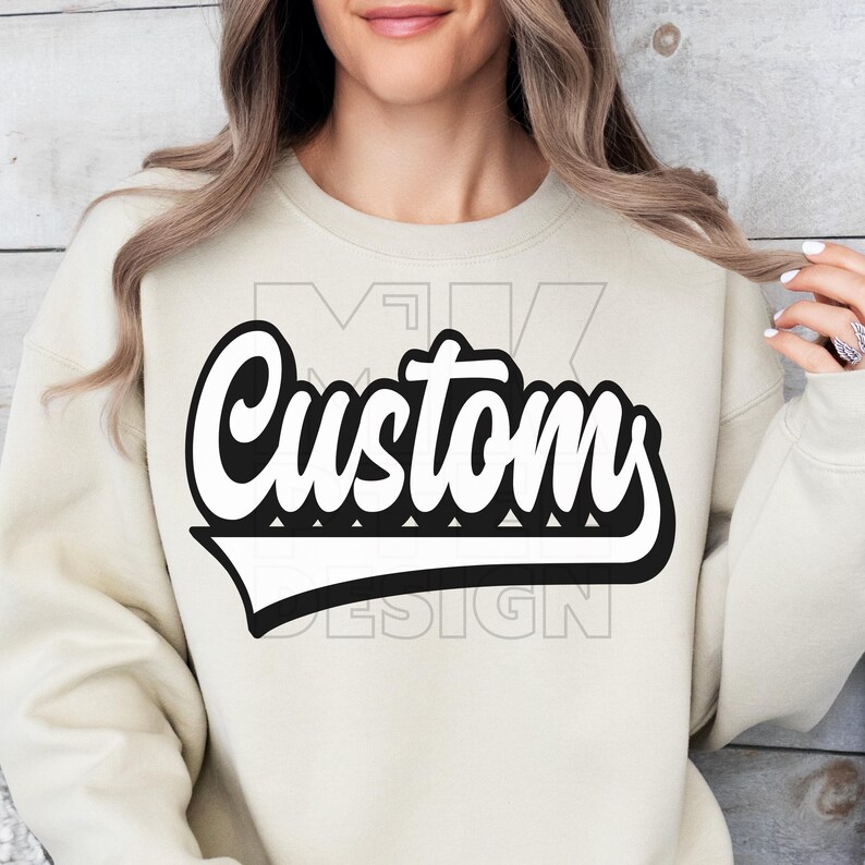 May include: A cream-colored sweatshirt featuring the word "Custom" in a bold, black and white, retro-style font. The design includes a black outline and a white drop shadow, creating a 3D effect. The sweatshirt has a crew neck and long sleeves.