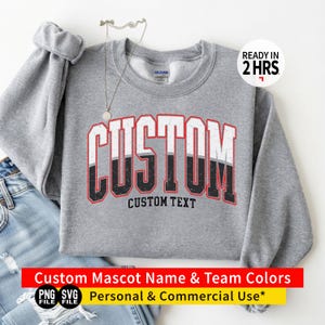 Op de afbeelding: Een grijs gemêleerd sweatshirt met ronde hals en het woord CUSTOM in grote, verweerde blokletters met een witte bovenkant en zwarte onderkant, omlijnd in rood. Daaronder staat de tekst CUSTOM TEXT in een kleiner zwart lettertype.