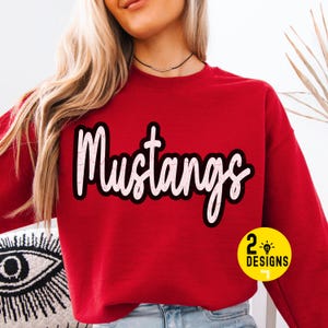 May include: A red sweatshirt with the word "Mustangs" in white script with a black outline. A small yellow circle with the text "2 Designs" is in the lower right corner. The sweatshirt is a crew neck style.