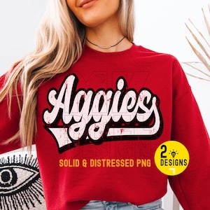 May include: A red sweatshirt with the word "Aggies" in a distressed white and black font. The sweatshirt also has the text "SOLID & DISTRESSED PNG" and a small graphic that says "2 DESIGNS".