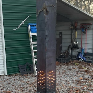 May include: A black metal fire pit with a square base and a tall, rectangular chimney. The chimney has a perforated section and is burning with orange flames. The fire pit is labeled "Dirt & Debris Farms" and "Custom Metal Work".
