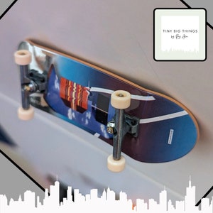 May include: A small skateboard with a vibrant graphic design showing a blue sky, clouds, and a building. It has silver trucks and cream-colored wheels. The text "TINY BIG THINGS by Ray Allen" is in the top right corner.