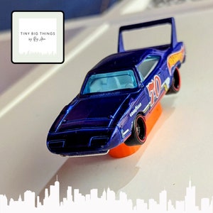 May include: A blue toy car with a white number "70" on the side. The car has a black spoiler and black wheels with "Goodyear" written on the tyres. The car is on a white surface.