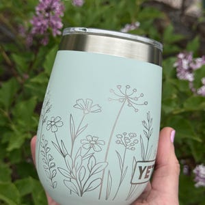 Peut inclure: Un gobelet isotherme vert menthe avec un bord et un couvercle argent&eacute;s. Le gobelet pr&eacute;sente un motif floral dans une teinte plus claire de vert. Le mot "YE" est visible sur le c&ocirc;t&eacute;. Le gobelet est tenu dans une main.