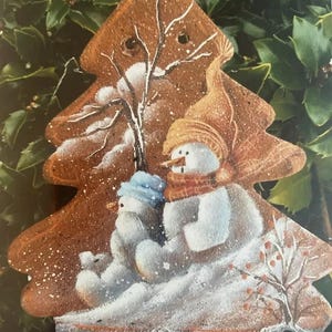 May include: A wooden Christmas tree ornament painted with two snowmen, one wearing a brown hat and the other wearing a blue hat. The tree is decorated with white snow and a brown tree trunk.