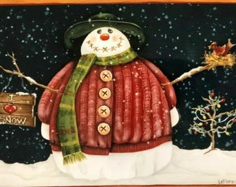 Puede incluir: Un muñeco de nieve con un suéter rojo con botones, una bufanda verde y un sombrero marrón. El muñeco de nieve sostiene un cartel que dice "Me encanta la nieve". El fondo es azul oscuro con copos de nieve blancos.