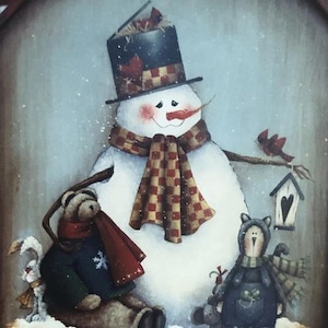 Puede incluir: Una escena invernal caprichosa con un muñeco de nieve con un sombrero de copa negro y una bufanda a cuadros. Un oso de peluche y una muñeca están sentados cerca del muñeco de nieve. También hay un pájaro pequeño y una casita para pájaros.