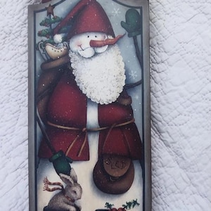 Puede incluir: Cartel de Navidad de madera con un muñeco de nieve disfrazado de Papá Noel, con nariz de zanahoria y barba blanca. El cartel tiene las palabras "Seasons Greetings" en la parte superior e incluye un conejo y un cardenal. El muñeco de nieve lleva un bolso y un pequeño árbol de Navidad.