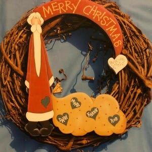 Puede incluir: Una corona de Navidad con un Papá Noel pintado, un corazón con las palabras "Feliz Navidad" y una nube con los nombres "Frank", "Karen", "Dave" y "Rob" pintados en ella.