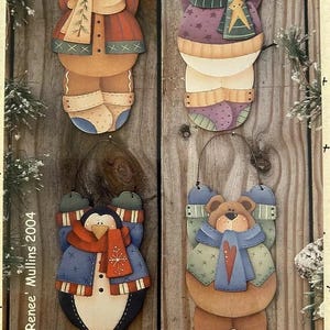 May include: Four wooden Christmas decorations hanging on a wooden background. The decorations are painted to look like a gingerbread person, a snowman, a penguin, and a bear. Each decoration is wearing a scarf and hat.