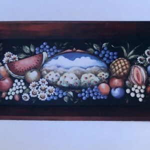 May include: Rectangular wooden serving tray with a dark brown frame and white handles. The tray's surface features a colorful still life of fruits, including watermelon, grapes, apples, and a pineapple, with a landscape scene in the center.