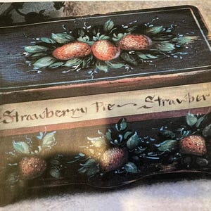May include: A rectangular, hand-painted wooden box with a black background. The box is decorated with strawberries and green leaves. The words "Strawberry Pie" are painted on the front of the box.