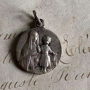 May include: Silver pendant featuring a religious image of the Virgin Mary and a child. The pendant is round and has a detailed design.
