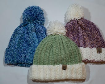 May include: Three knitted winter hats with pom-poms. One hat is blue and white, one is green and white, and one is purple and white.