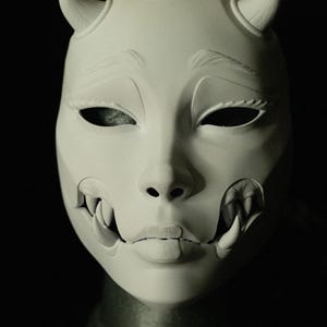 May include: A white mask with a demonic design, featuring curved horns, sharp teeth, and detailed facial features. The mask has a smooth texture and is set against a dark background. The text "THE LAIR Le Terrier" is visible at the bottom.