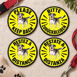 Puede incluir: Cuatro parches circulares amarillos con bordes negros, cada uno con el gráfico de un perro gris y blanco con collar rojo. El texto dice: PLEASE KEEP BACK, BITTE ZURÜCKBLEIBEN, RESTEZ À DISTANCE y RESTATE A DISTANZA en letras negras negritas.