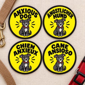 Könnte beinhalten: Vier kreisförmige gelbe Aufnäher mit schwarzem Rand, die jeweils eine Cartoon-Illustration eines grauen Hundes mit rotem Halsband zeigen. Der Text auf den Aufnähern lautet ANXIOUS DOG, ÄNGSTLICHER HUND, CHIEN ANXIEUX und CANE ANSIOSO.