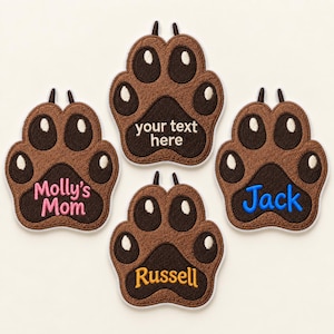 Op de afbeelding: Vier bruine geborduurde pootafdruk-patches met donkerbruine kussentjes en witte accenten. Eén patch bevat de tekst 'your text here', één zegt 'Molly's Mom' in roze, één zegt 'Jack' in blauw en één zegt 'Russell' in geel borduurwerk.