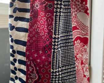 May include: A patchwork tote bag with a denim handle. The bag is made of different fabrics with red, white and blue patterns.