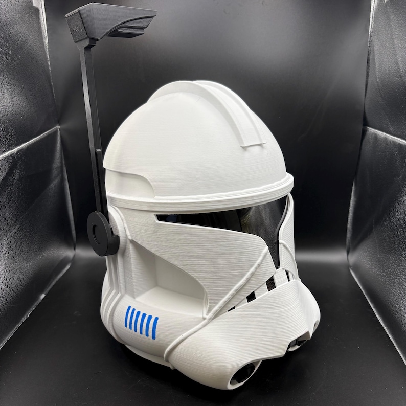 May include: White Clone Trooper helmet with a black visor and antenna. The helmet features blue markings and a detailed design. The helmet is made of a textured material, reminiscent of a Star Wars Clone Trooper.